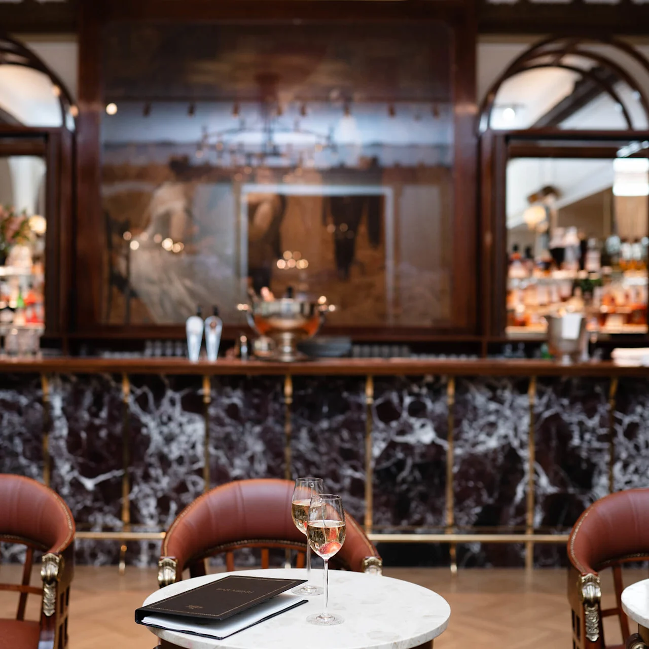 A glass of wine sits on a marble table, with elegant chairs and a posh bar in the background.