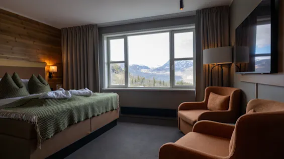 Ett mysigt hotellrum med en stor säng, två fåtöljer och en fantastisk utsikt över bergen från fönstret.