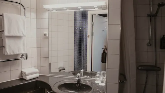 Valoisa ja kutsuva kylpyhuone Home Hotel Uppsalassa, varustettuna pesualtaalla, peilillä, puhtailla pyyhkeillä ja suihkulla.