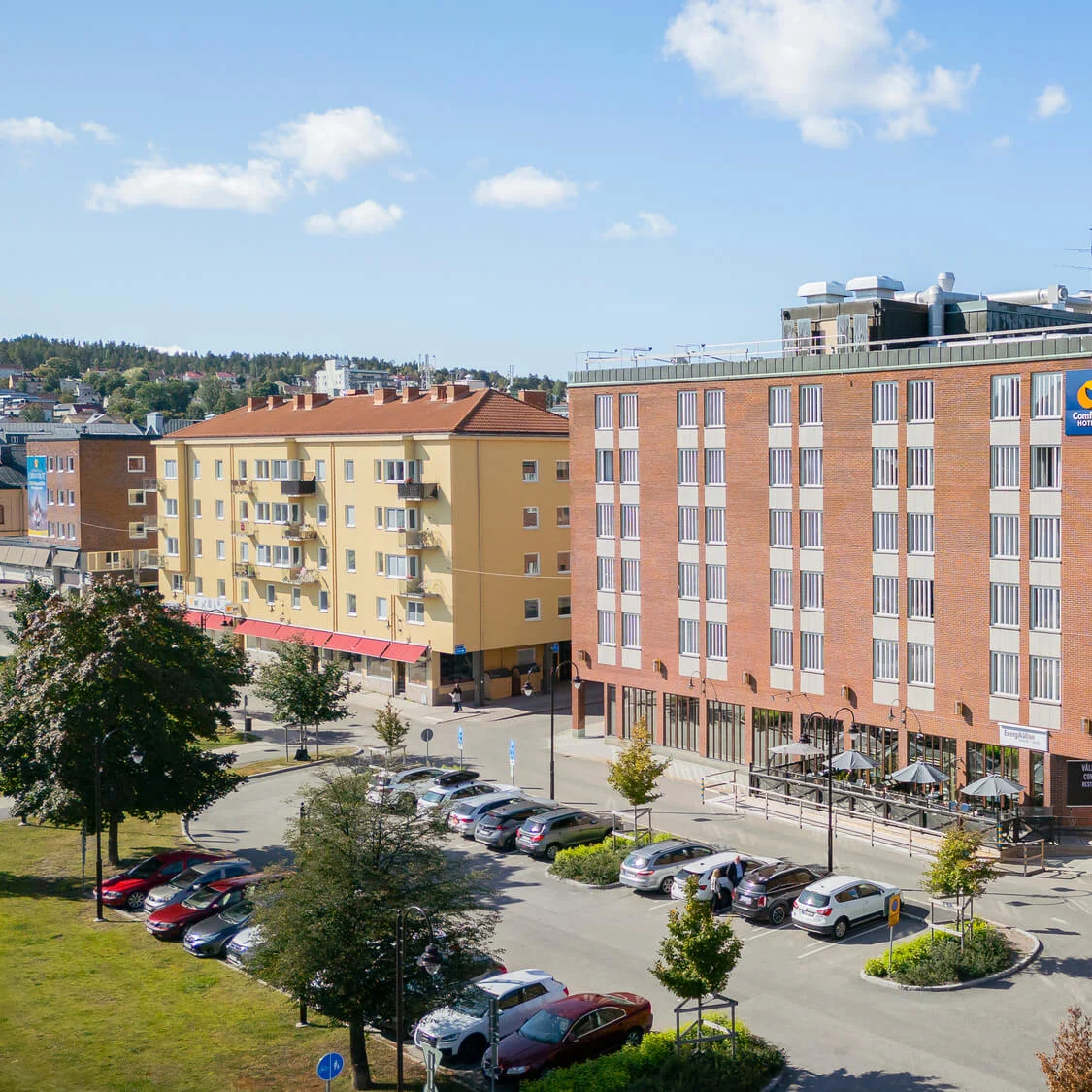 Modernt bebyggda hus och parkerade bilar, soligt stadsmiljö med blå himmel.