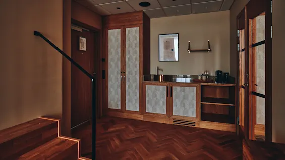 En innbydende hotellromsinngang med tretrapper, minibarområde og varm belysning.