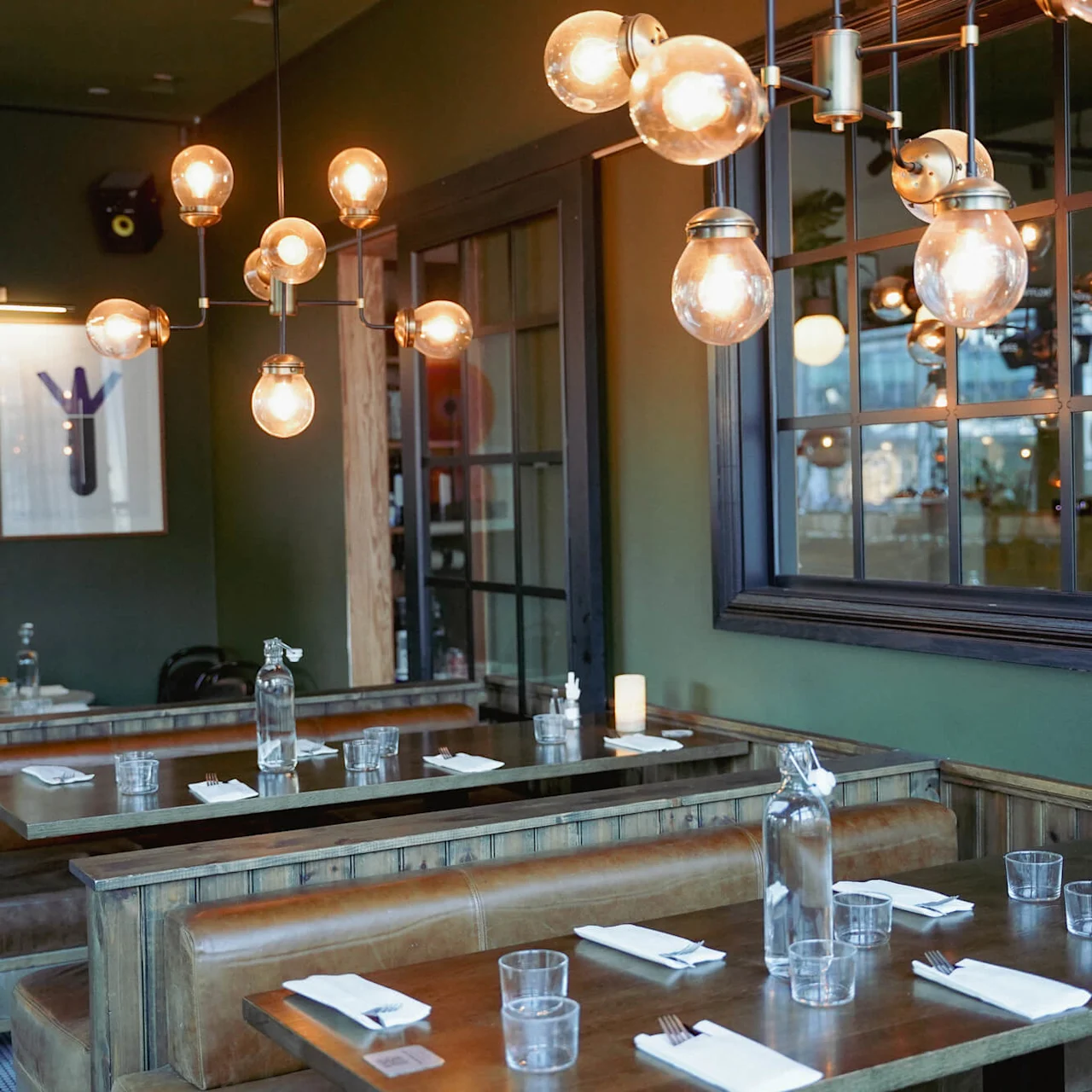 Varme lysarmaturer hænger over træborde dækket til spisning i et tomt restaurantinteriør.