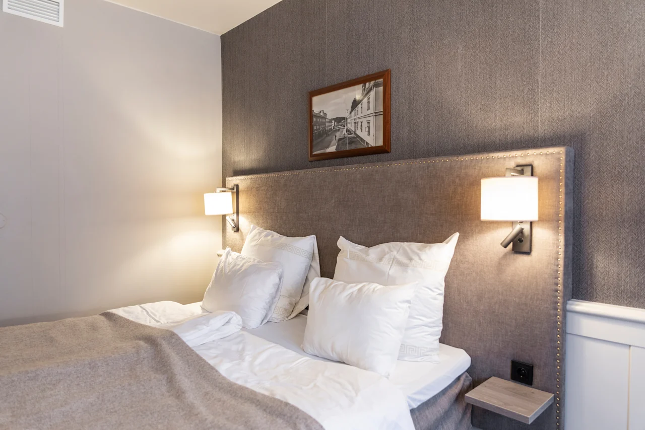 A comfortable and inviting hotel room at Home Hotel Grand Bodø, featuring a neatly made bed with white linens and soft lighting.