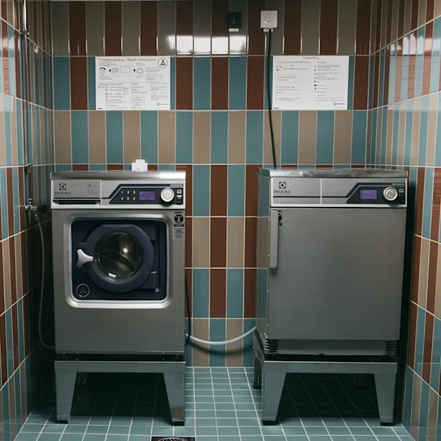 Ett rent tvättstuga med randiga kakel, med en tvättmaskin och torktumlare. Instruktioner för Tvättanvisning och Torkning är uppsatta.