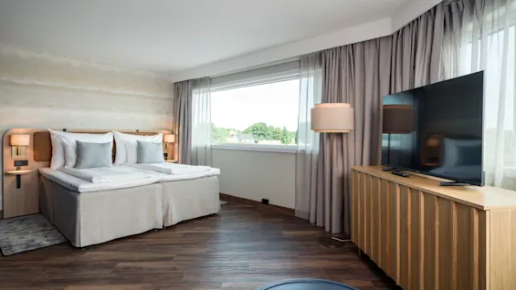 A modern hotel room with a comfortable bed, a large window offering natural light, and a television for entertainment.