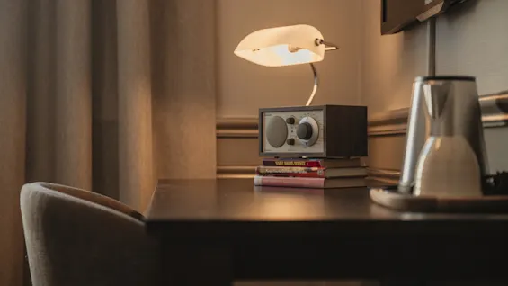 En mysig skrivbordsuppsättning med en varm lampa, en radio på böcker och en vattenkokare, redo för en avkopplande stund.