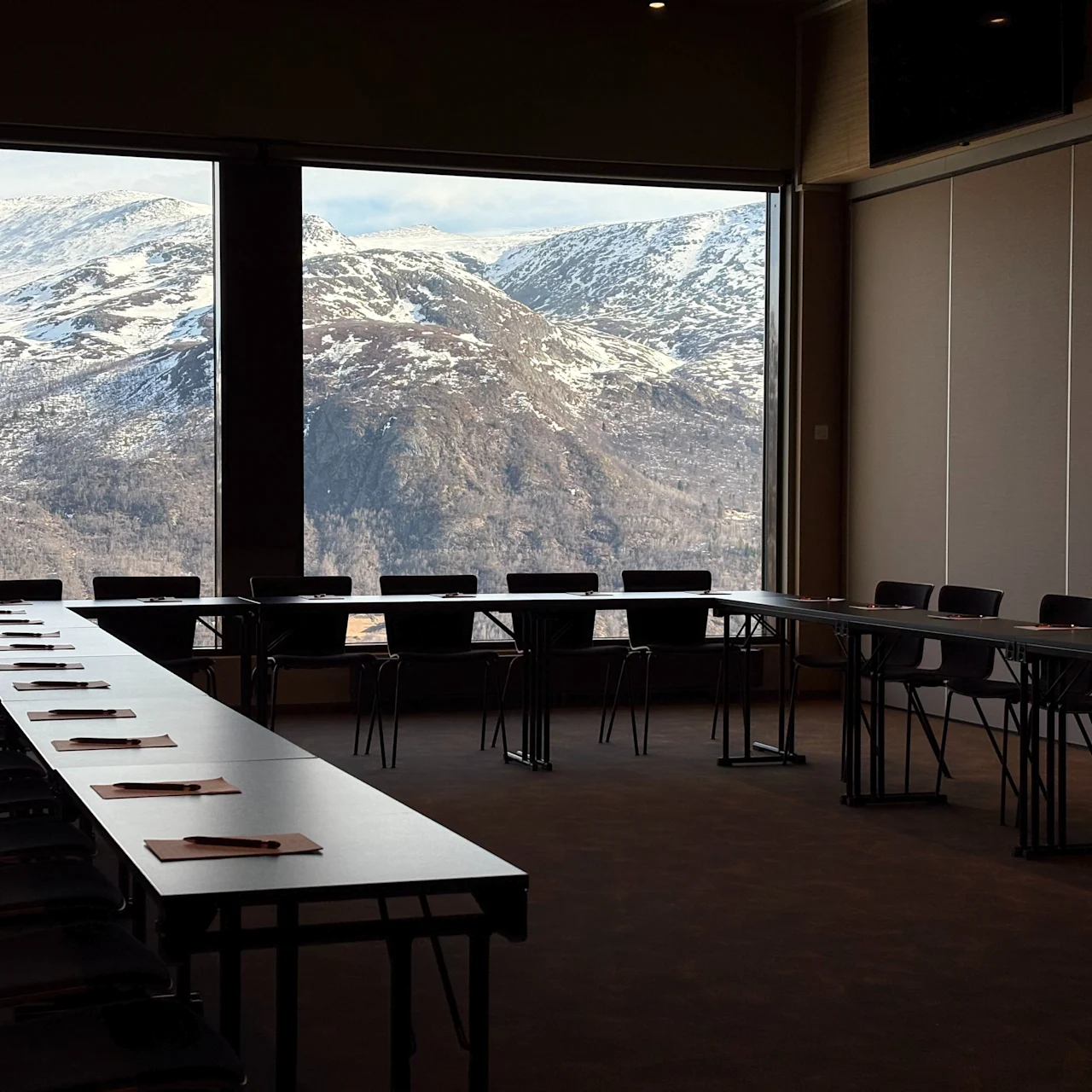 Conference room with arranged tables and chairs facing large windows, overlooking a snowy mountain landscape, creating a peaceful and inspiring atmosphere.