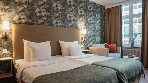 Et hyggeligt hotelværelse på Home Hotel Wellington med to senge, en mønstret væg og et behageligt siddeområde ved vinduet.