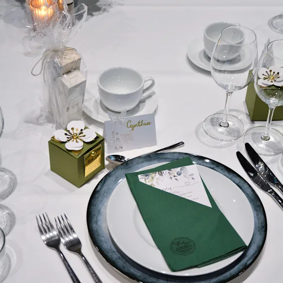 En vakkert arrangert borddekking for et formelt arrangement, komplett med elegant servise, grønne servietter, en meny og blomsterdekor.