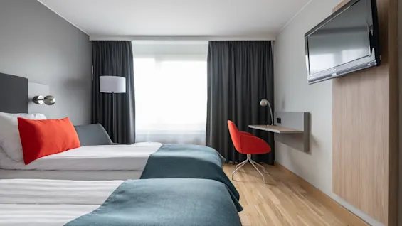 Mukava ja moderni hotellihuone Quality Hotel Prismassa, jossa on kaksi sänkyä, työpöytä ja seinälle asennettu televisio.