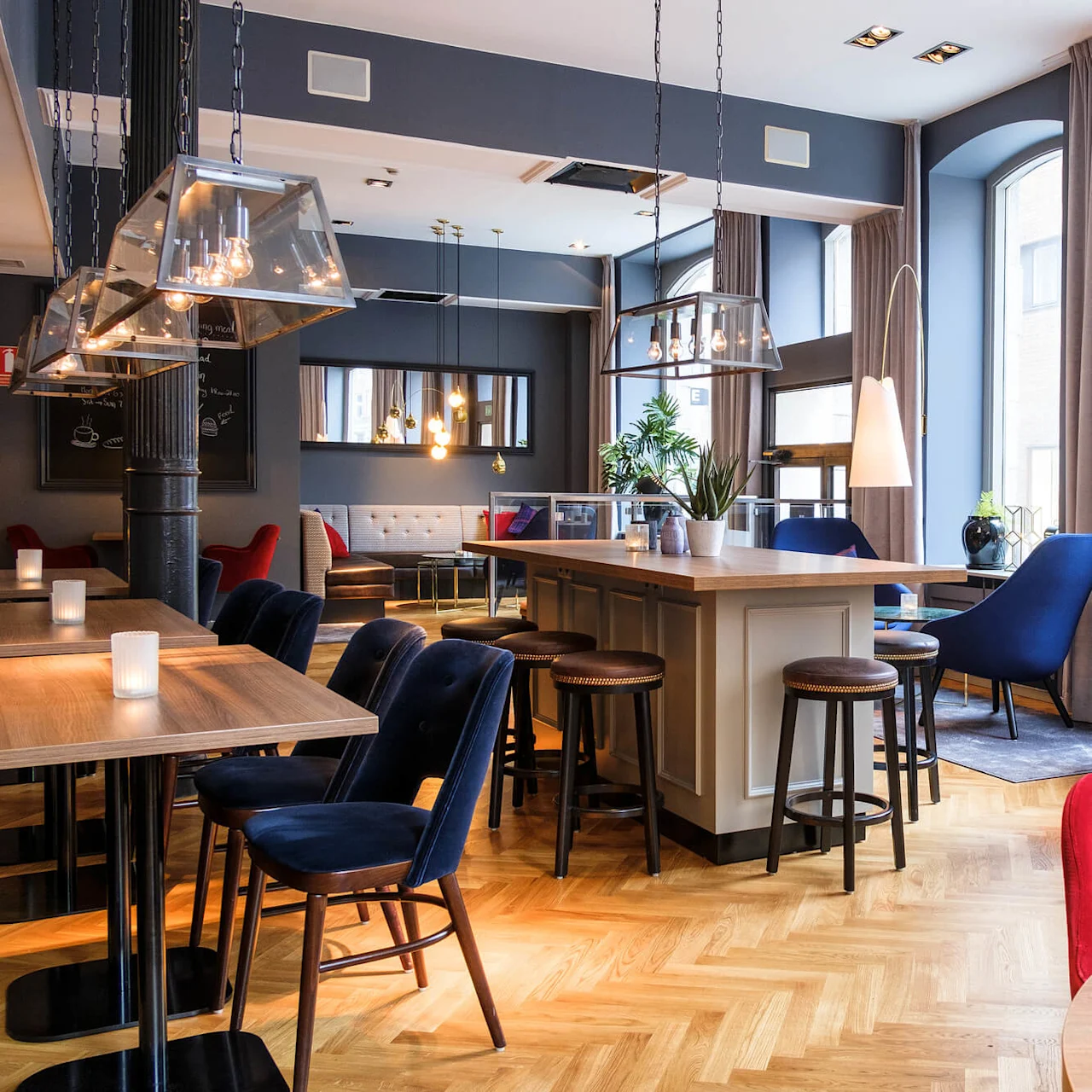 An elegant lounge with mixed seating including red and blue chairs, under stylish pendant lighting, reflecting a modern, cozy interior.