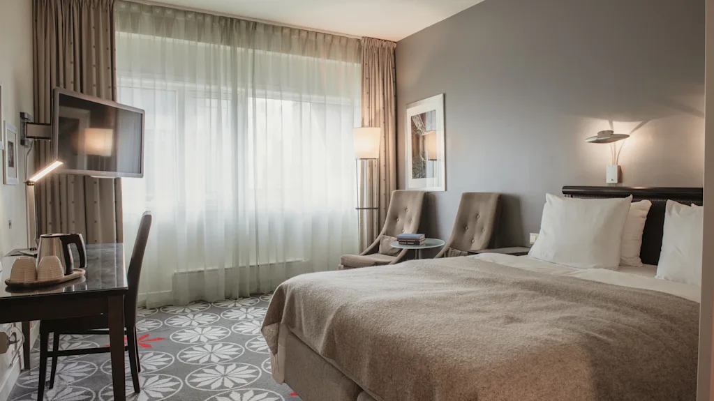 Ett mysigt hotellrum med en bekväm säng, en skrivbordshörna och en sittgrupp vid ett stort fönster.