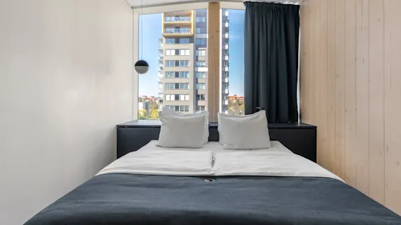 Et moderne hotelværelse med en komfortabel seng, et stort vindue med udsigt over byen og stilfuld indretning.