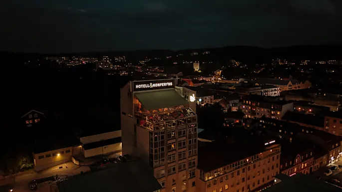 En by om natten, med en lyst opplyst hotell- og konferansebygning i forgrunnen. Bylysene glitrer i det fjerne.