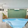 En lugn inomhuspool vilar stillsamt, omgiven av solstolar och krukväxter mot vitkaklade väggar. Den fridfulla miljön är mjukt upplyst under ett gallerformat tak.