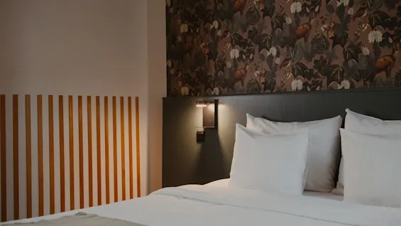 A cozy hotel room at Home Hotel Uppsala with a bed, white linens, and a nature-themed wallpaper.