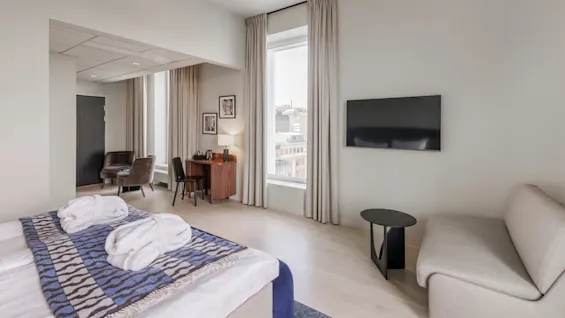 A neatly arranged hotel room with a made bed, a mounted TV, and a sitting area, suggesting a comfortable stay.