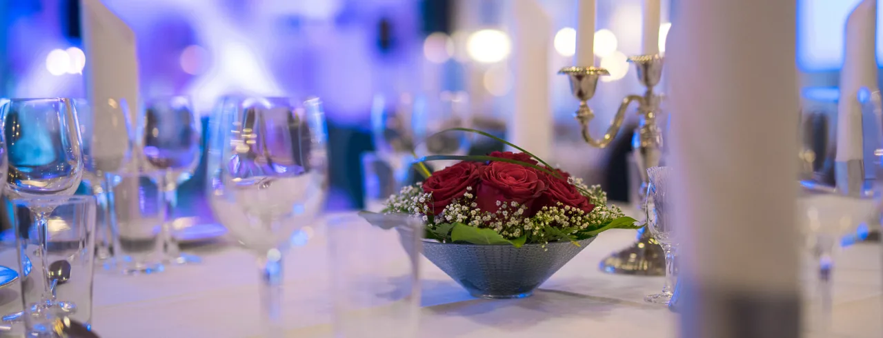 Detaljer fra et bord dekket med hvit duk, glass, blomsterdekorasjon og lysestake på Quality Hotel Olavsgaard