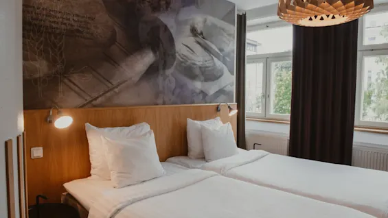 A cozy hotel room at Home Hotel Uppsala with two beds, white linens, and a wooden headboard. A wall mural features the word AGARE.