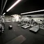 Treadmills line the mirrored wall, stationary in an empty gym. Dumbbells and exercise balls rest on padded floors under bright ceiling lights.