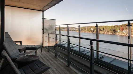 A balcony at Farris bad with lounge chairs overlooking a serene water view and distant green shores.