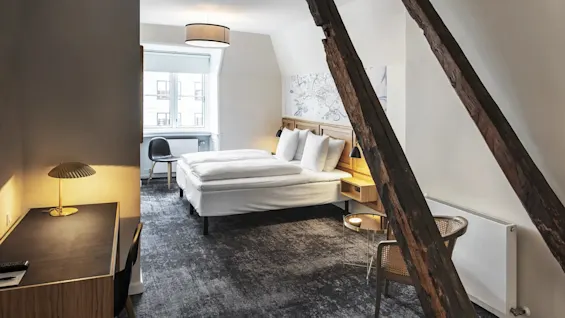 Et hyggeligt hotelværelse med en komfortabel seng, et skrivebord og rustikke træbjælker, der tilbyder en varm og indbydende atmosfære.