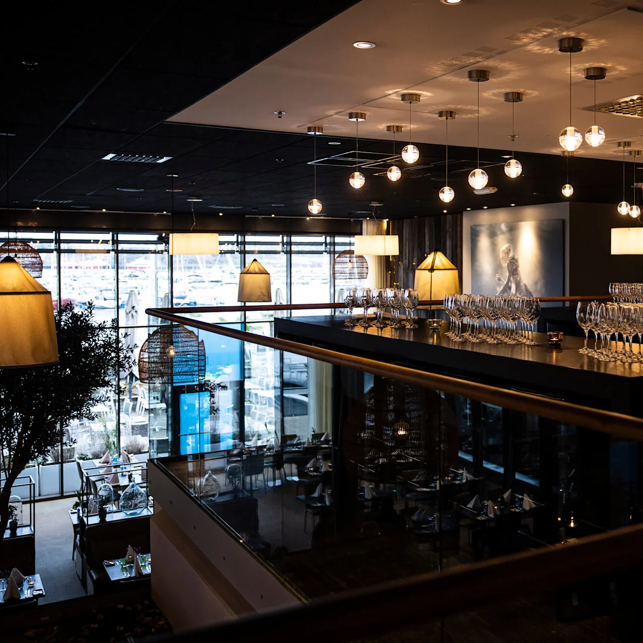 Glass plassert på en bardisk under moderne hengelamper. Innstillingen er en svakt opplyst, eksklusiv restaurant med store vinduer og stilig dekor.
