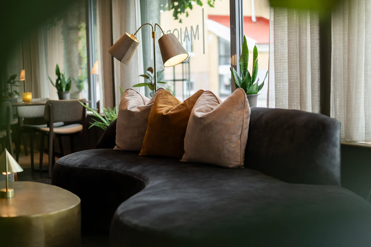 An inviting lounge area with a dark curved sofa, plush pillows, and warm lighting, perfect for relaxation.