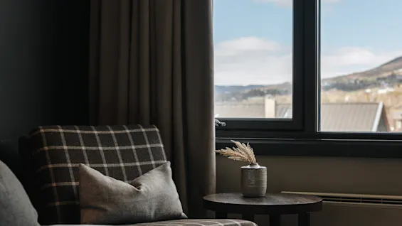 Mysigt hotellrum med en rutig fåtölj vid ett fönster med utsikt mot bergen.