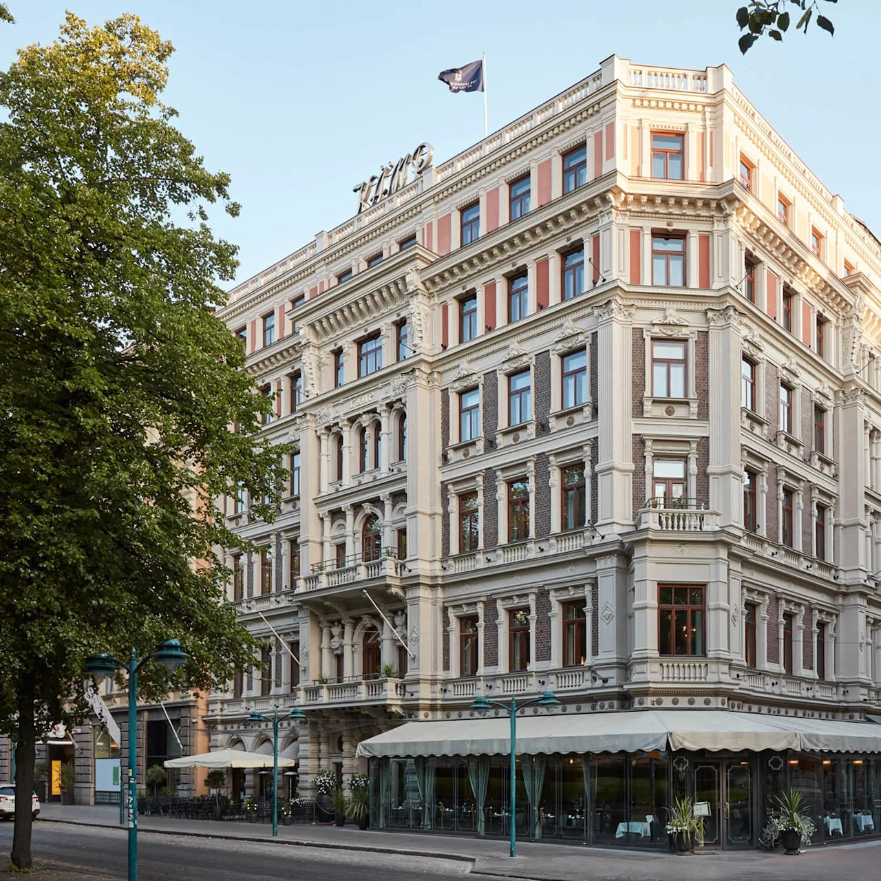 Elegant corner building with a café at street level, set in an urban environment with trees and clear skies.