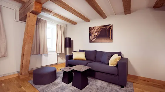 En koselig stue med en mørk grå sofa pyntet med gule puter, synlige trebjelker, og moderne dekor.