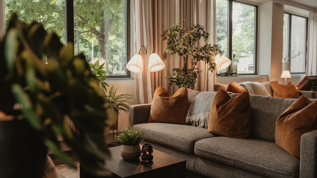 A cozy lounge area with comfortable sofas, warm lighting, and large windows looking out onto lush greenery.