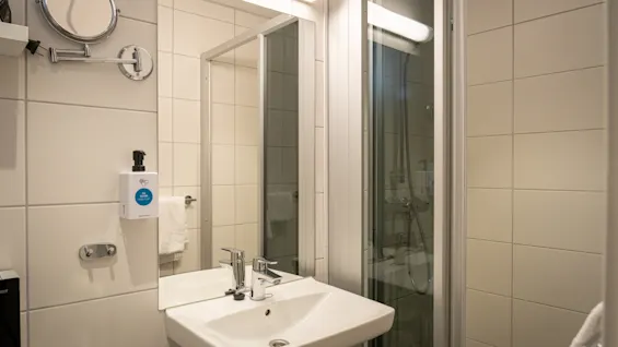 A clean, modern bathroom with a sink, mirror, and shower. A soap dispenser on the wall reads "GO CLEAN PROTECT".