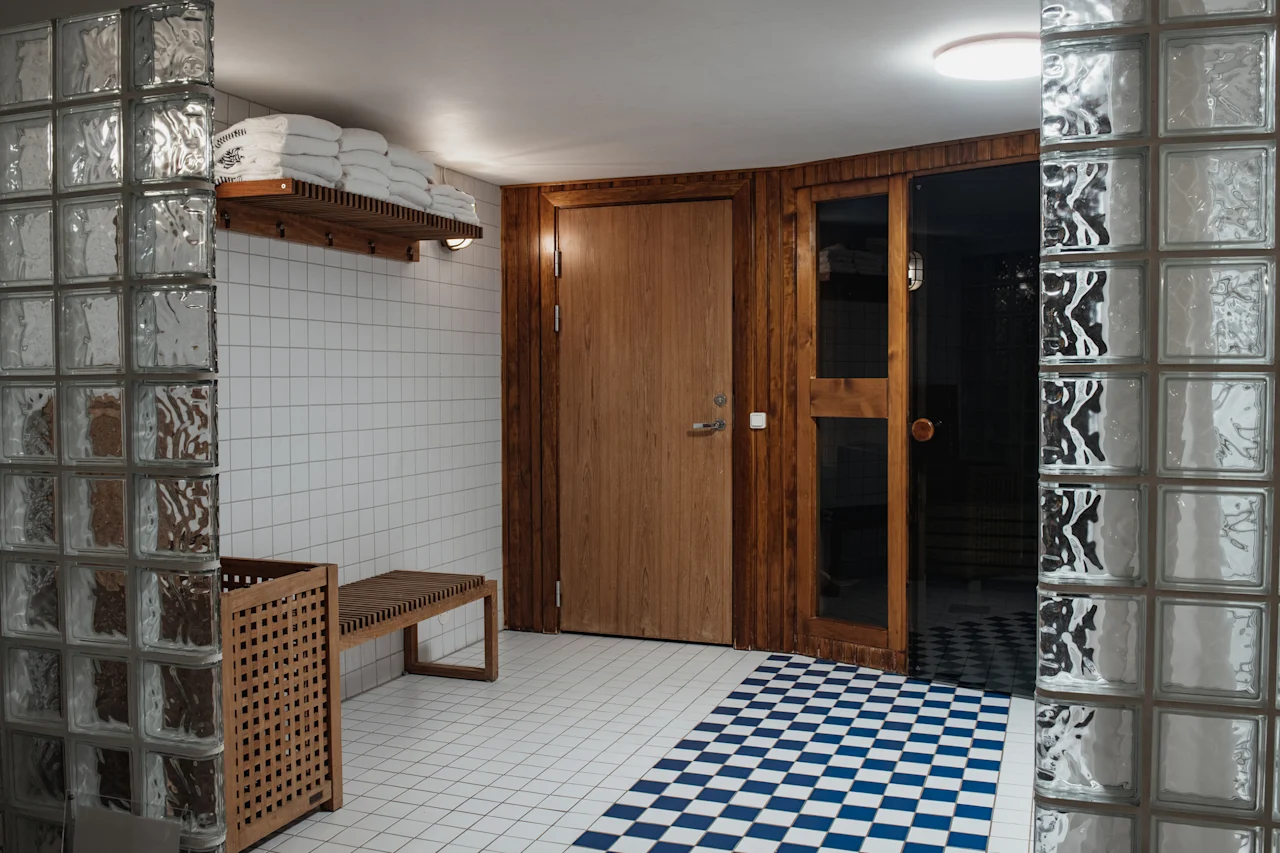 Home Hotel Kung Oscar. A clean and inviting spa changing area with fresh towels, a wooden bench, and a sauna entrance.