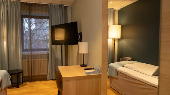 A cozy hotel room with a desk, TV, and a comfortable bed reflected in a mirror, ready for a relaxing stay.