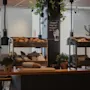 Viihtyisä aamiaisbuffet, jossa on erilaisia leipiä ja leivonnaisia puulaatikoissa, pinottuja lautasia ja allergiakyltti.