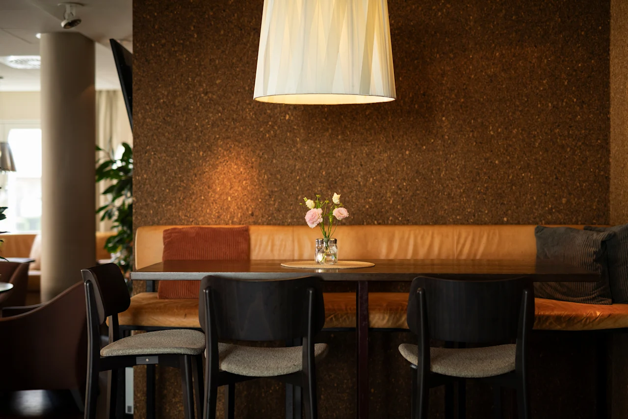 Mysig sittgrupp på Home Hotel Tapto med ett långt bord, bekväm bänk och ett blomsterarrangemang.