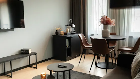 Et stilfullt og koselig hotellrom med spiseplass med rundt bord og en salongdel med sofa og TV.