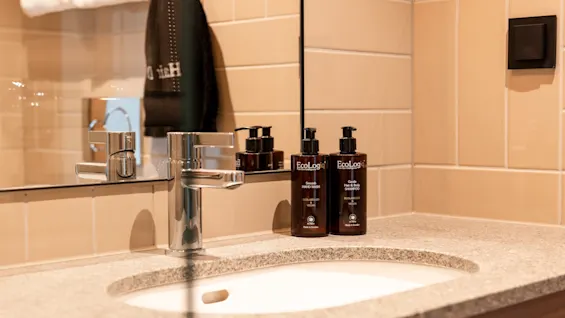 A modern bathroom sink at Quality Hotel The Book with Smooth HAND WASH and Gentle Hair & Body SHAMPOO bottles, reflecting a towel.