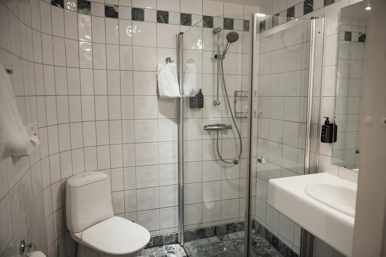 Et rent og moderne hotellbad med toalett, en dusjkabinett i glass og en vask med toalettartikler.
