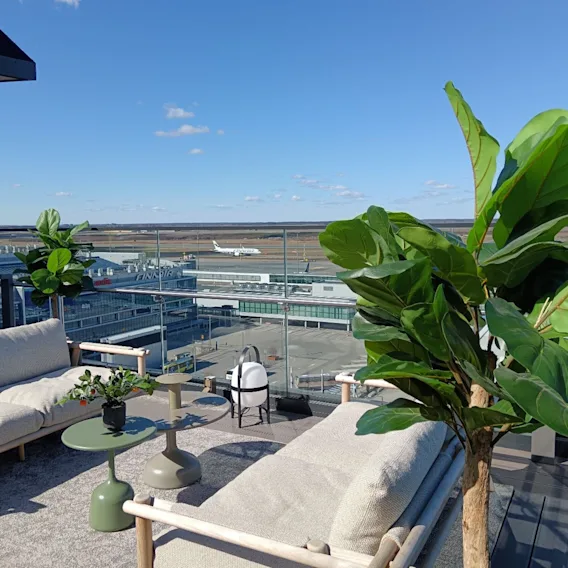 Clarion Hotel Helsinki Airportin kattoterassi oleskeluryhmineen ja kasveineen, josta on näkymä lentokentän kiitotielle ja lentokoneeseen.