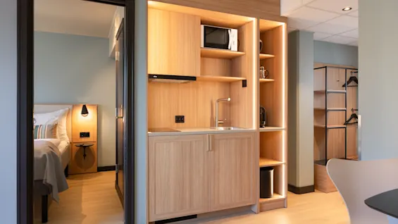 Ett modernt hotellrum med ett kompakt pentry med träskåp, diskho och mikrovågsugn, intill ett mysigt sovrum.