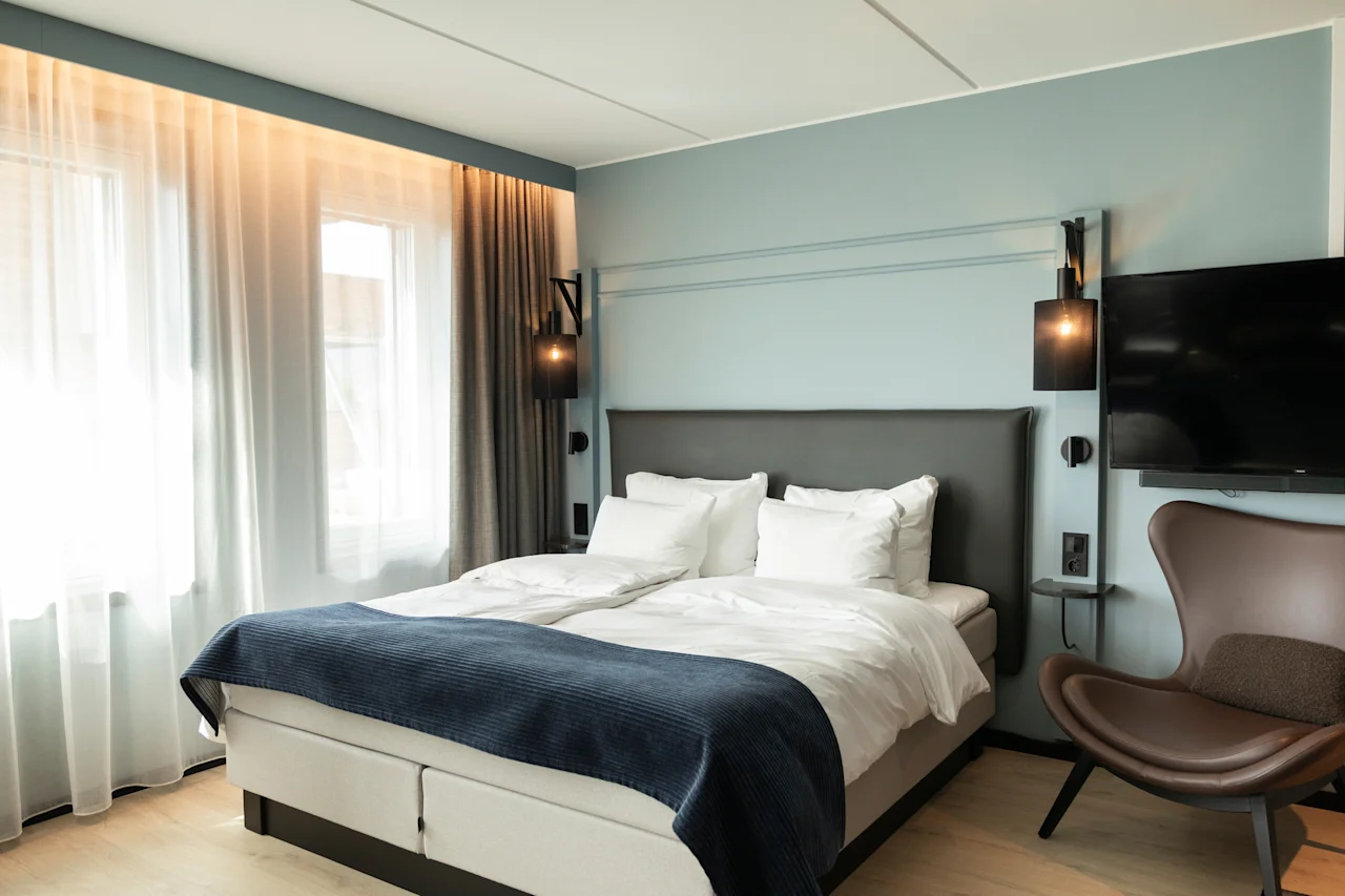 Et moderne og innbydende hotellrom med en komfortabel seng, en koselig lenestol og en flatskjerm-TV.