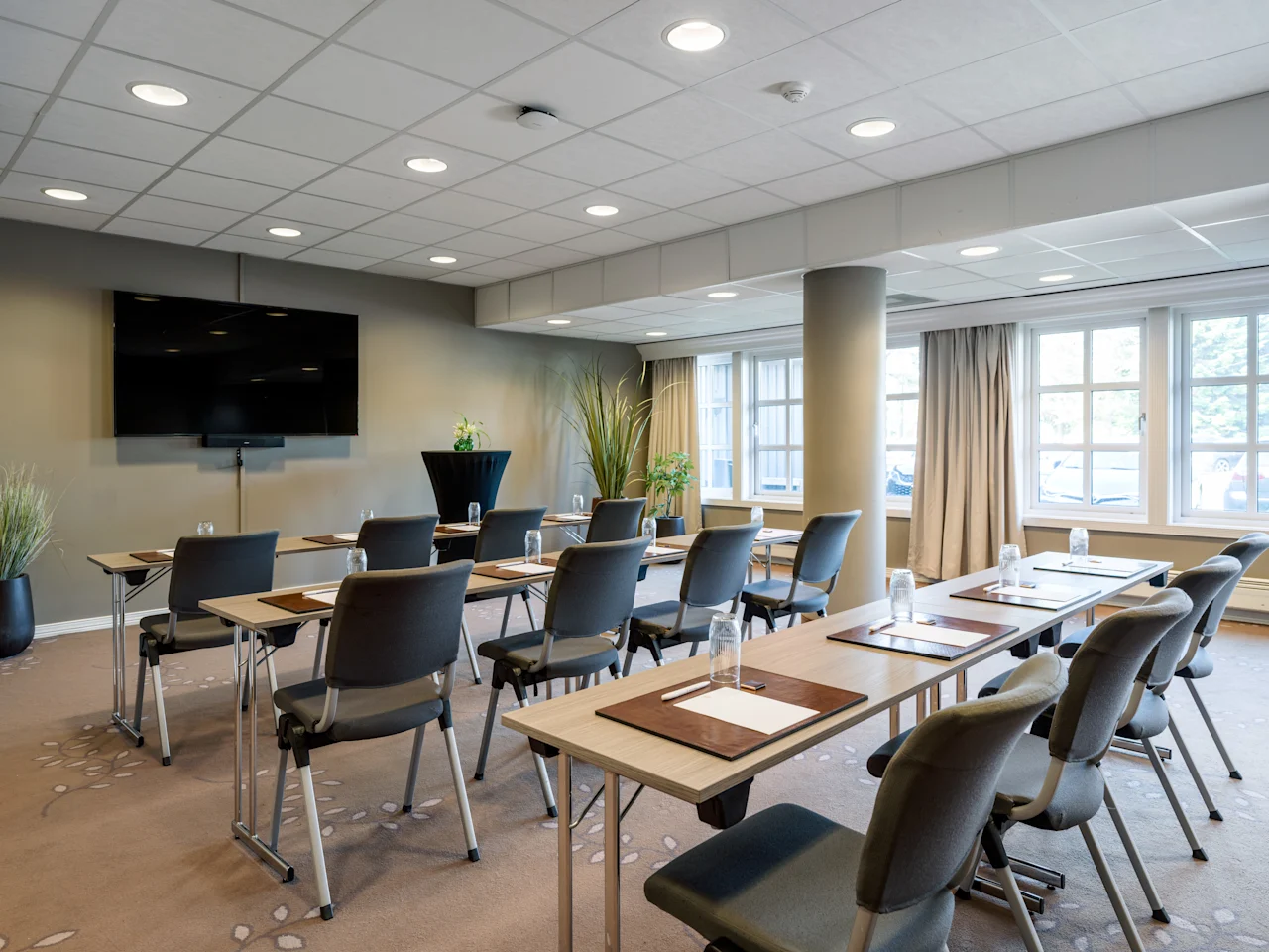 Ett modernt konferensrum med rader av bord och stolar vända mot en stor skärm, redo för ett möte eller en presentation.