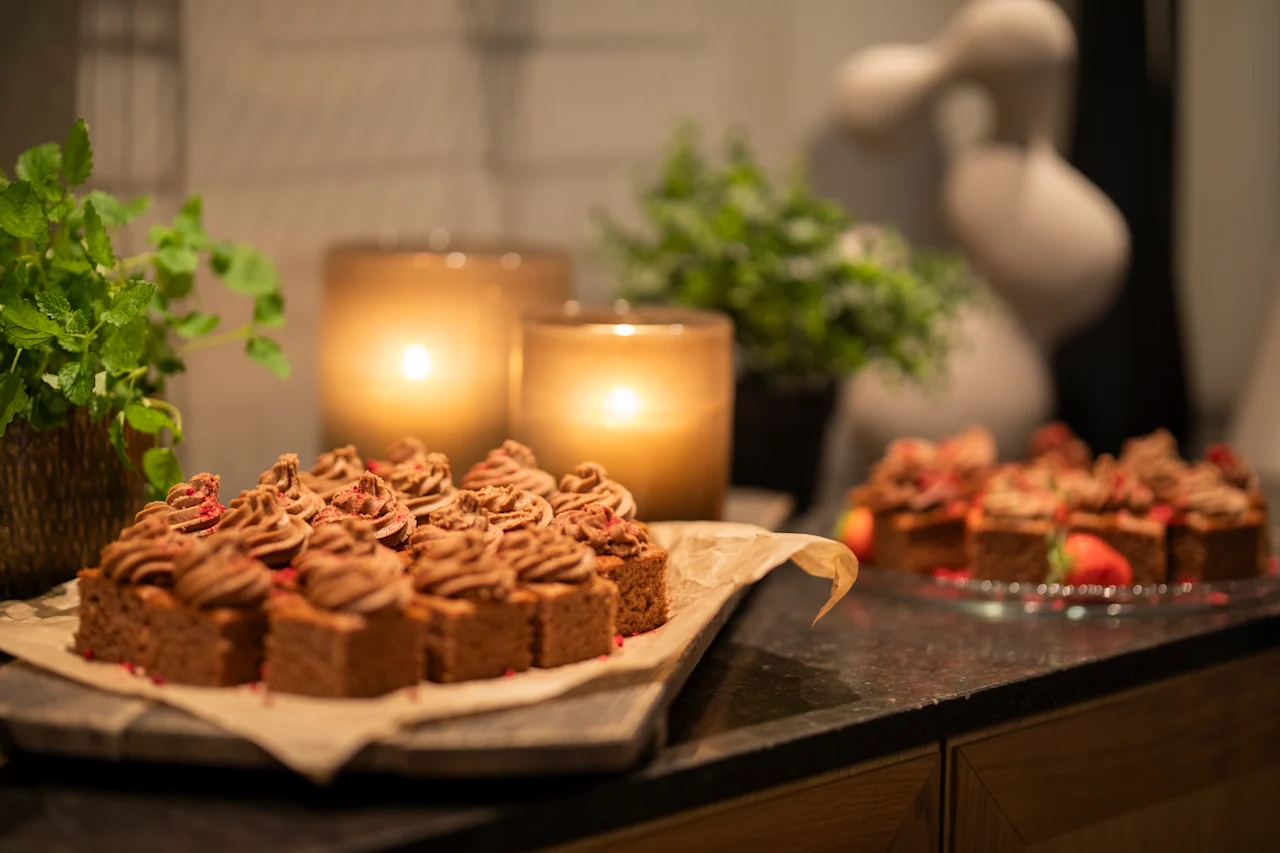 Sjokolademuffins med virvlet glasur hviler på et fat. To tente stearinlys og potteplanter pynter den mørke overflaten, og skaper en varm, innbydende atmosfære.