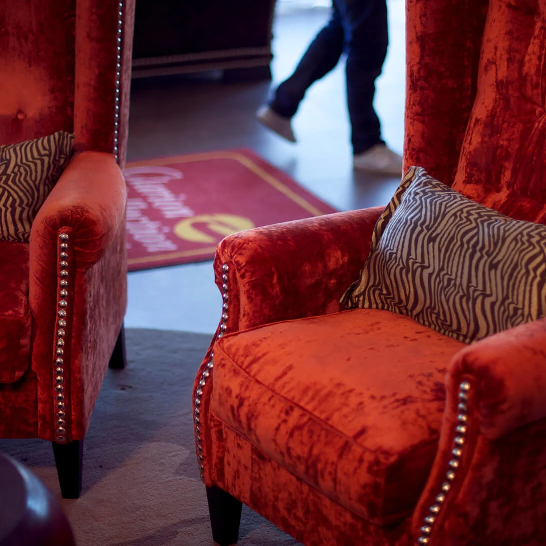 Two plush red armchairs with a zigzag patterned pillow, situated in an intimate lounge setting with low lighting.