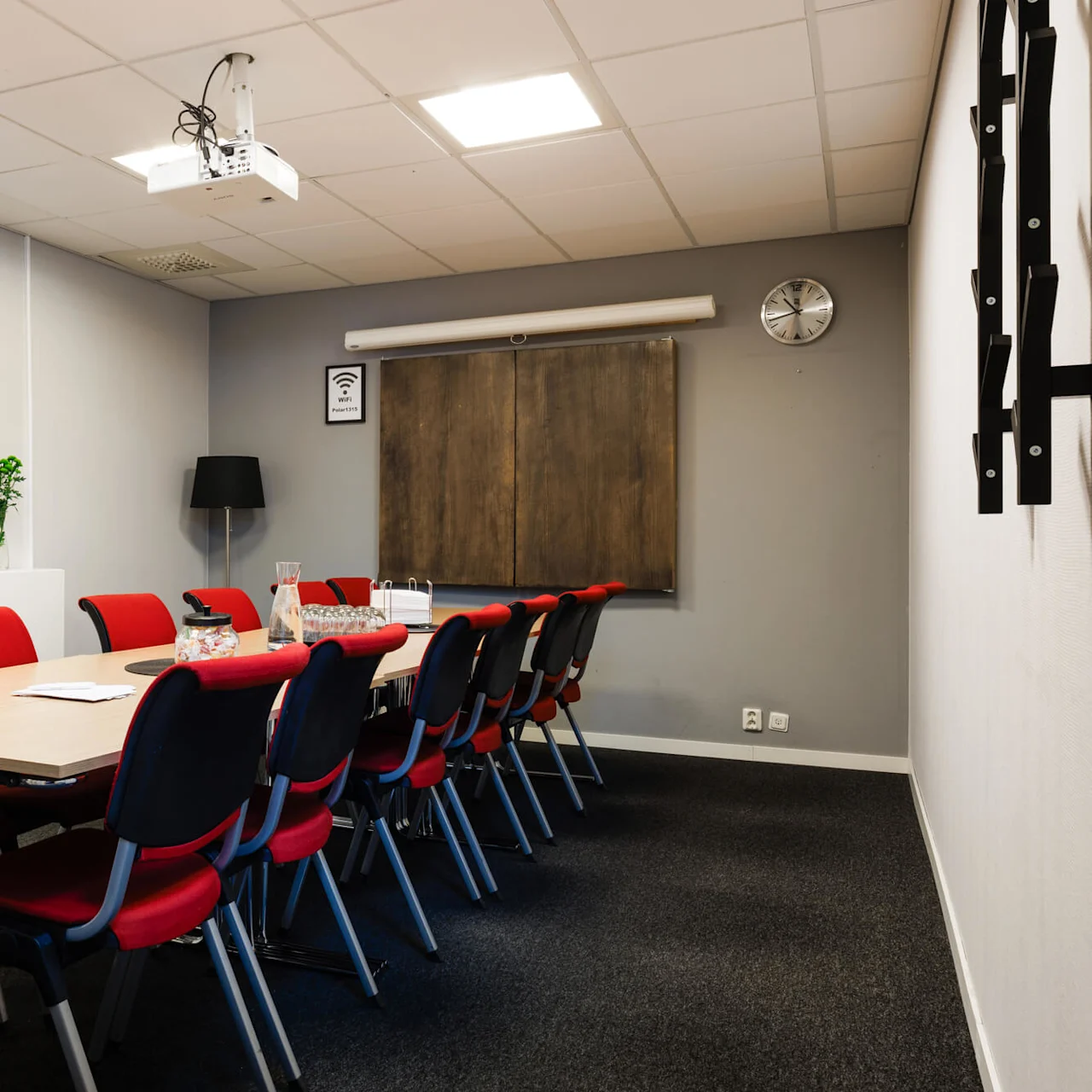 Mötesrum med ett långt bord och röda stolar, utrustat med en takprojektor. En karta märkt "BODEN" och en WiFi-skylt finns på väggarna.