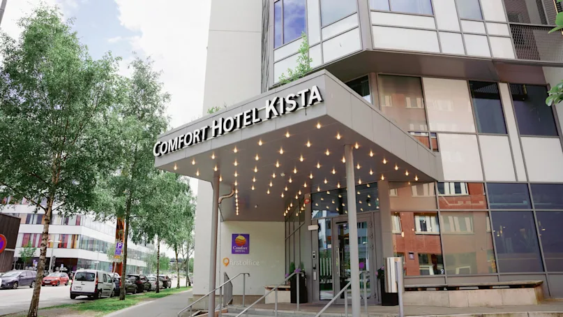 Hotel entrance with a canopy lined with lights, trees on the side, in a city setting.