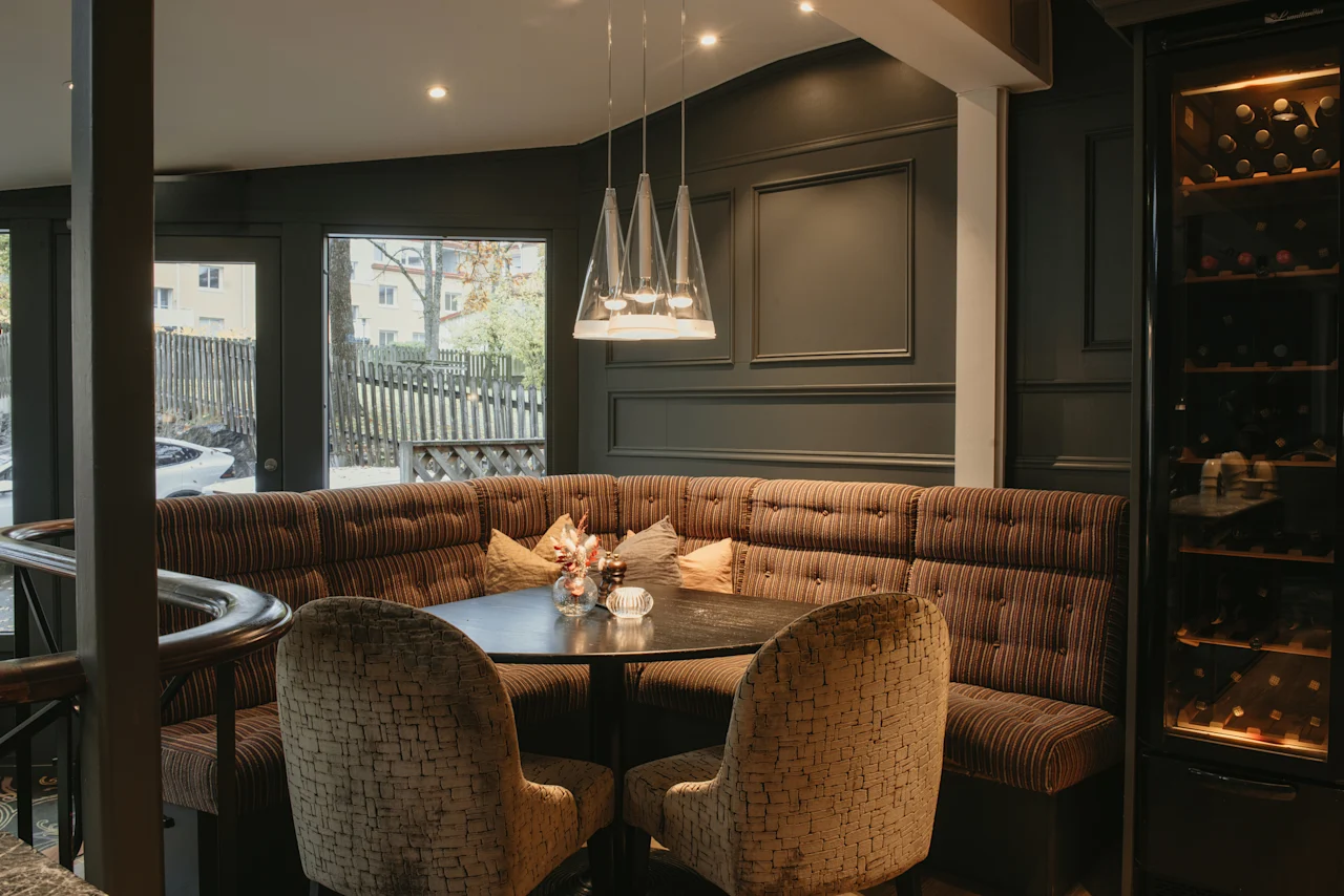 A cozy dining nook at Home Hotel Kung Oscar with a round table, upholstered seating, and a wine cooler.