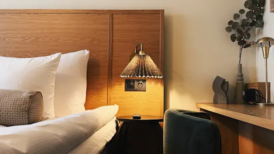 Ett mysigt hotellrum med en bekväm säng, en varm sänglampa och en stilren skrivbordsplats, perfekt för avkoppling eller arbete.